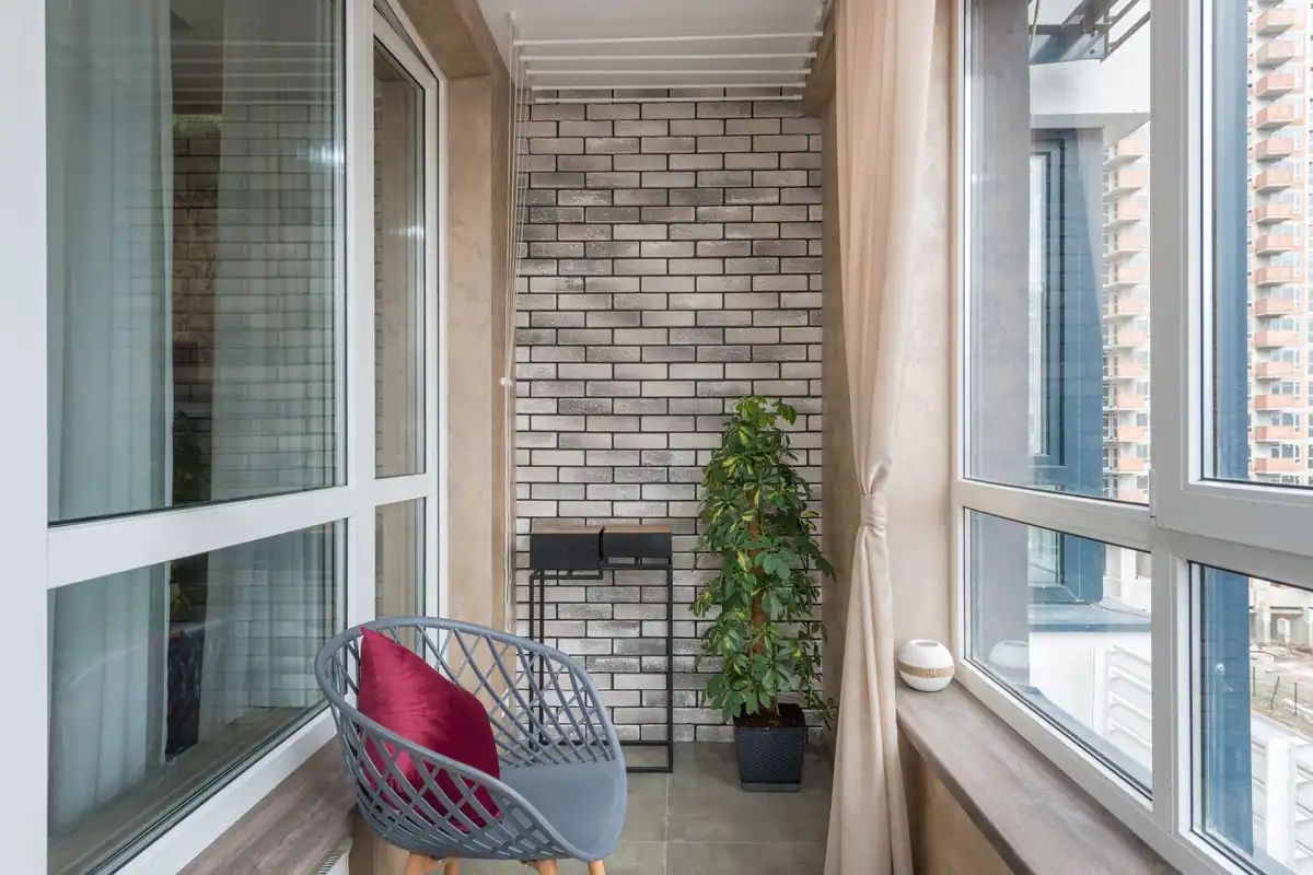 Scaun cu pernă și plantă în ghiveci pe o terasă luminoasă de apartament