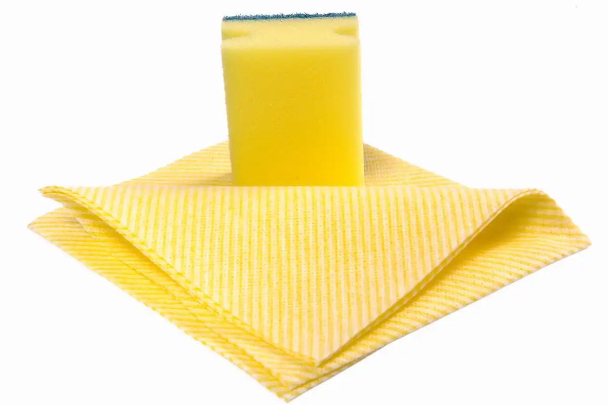 Mână cu mănușă de latex ținând un burete pentru curățenia băii, alături de lămâie și produse de curățat