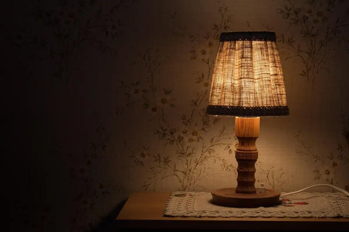Veioză cu abajur din material textil pe noptieră, cu lumină caldă într-un dormitor